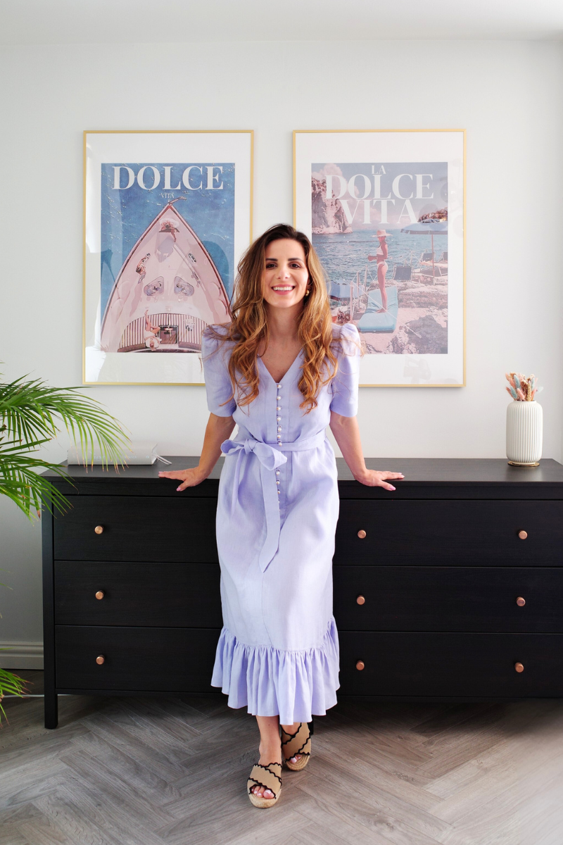Woman in a light purple dress standing in a room with framed pictures on the wall.