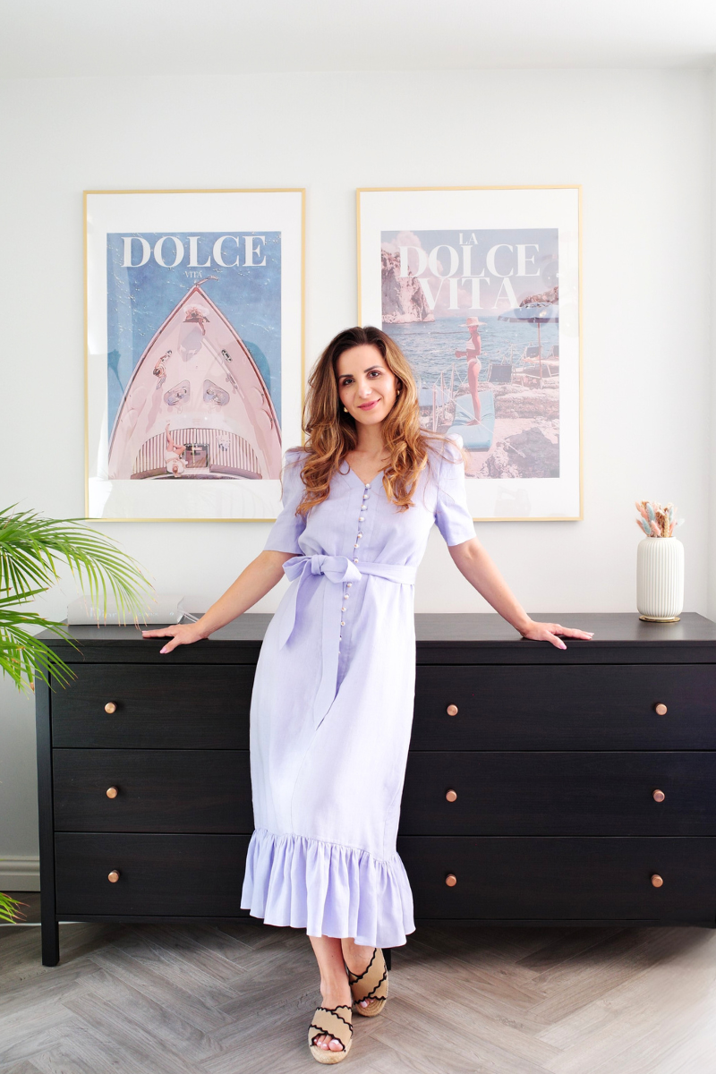 Woman in a light purple dress standing in a room with Dolce posters on the wall.