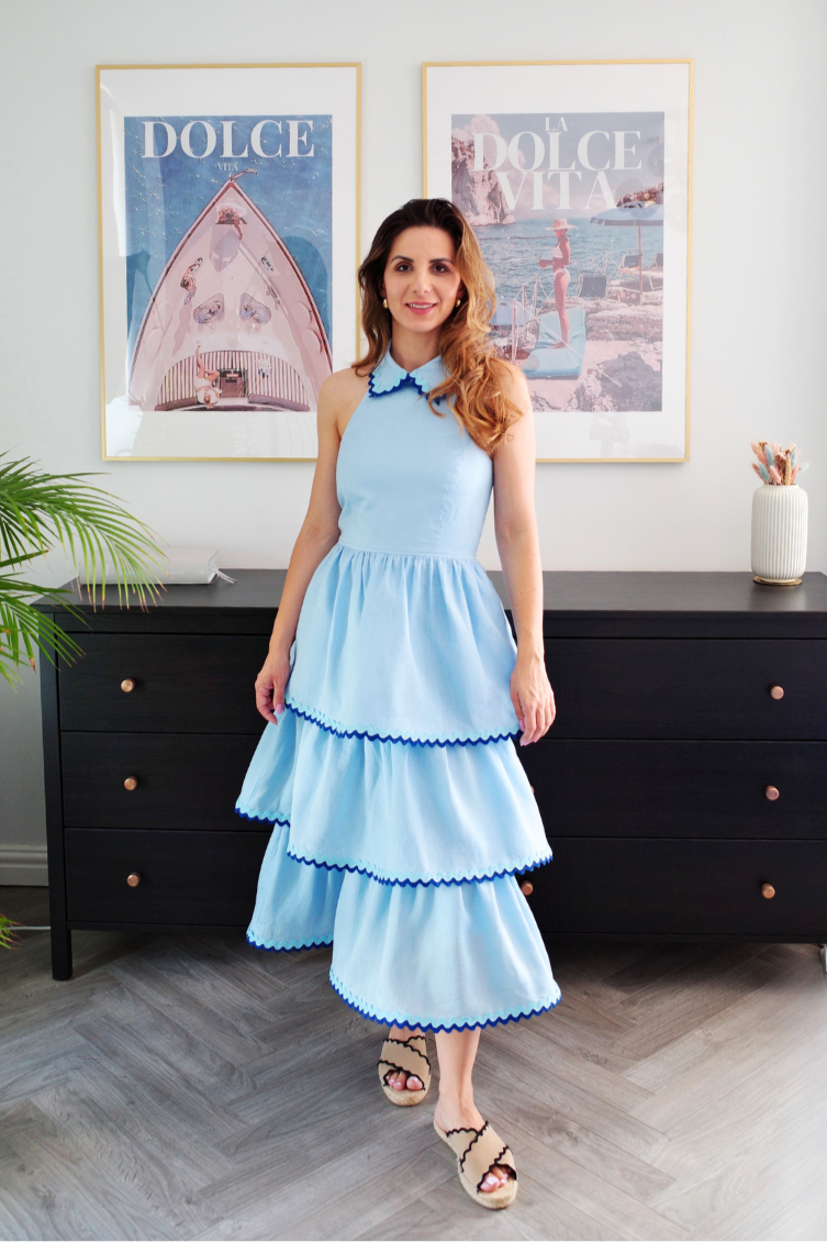 Woman in a light blue dress standing in a room with black furniture and framed pictures on the wall.