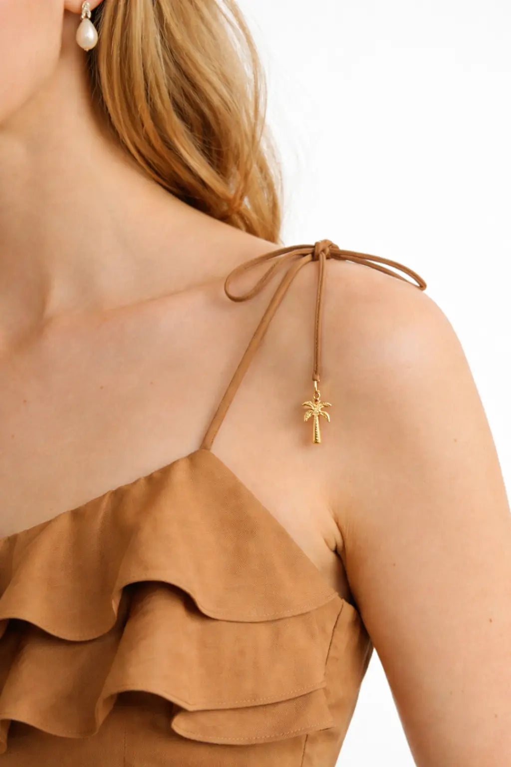 Close-up of a person wearing a brown dress with a gold palm tree earring on a white background