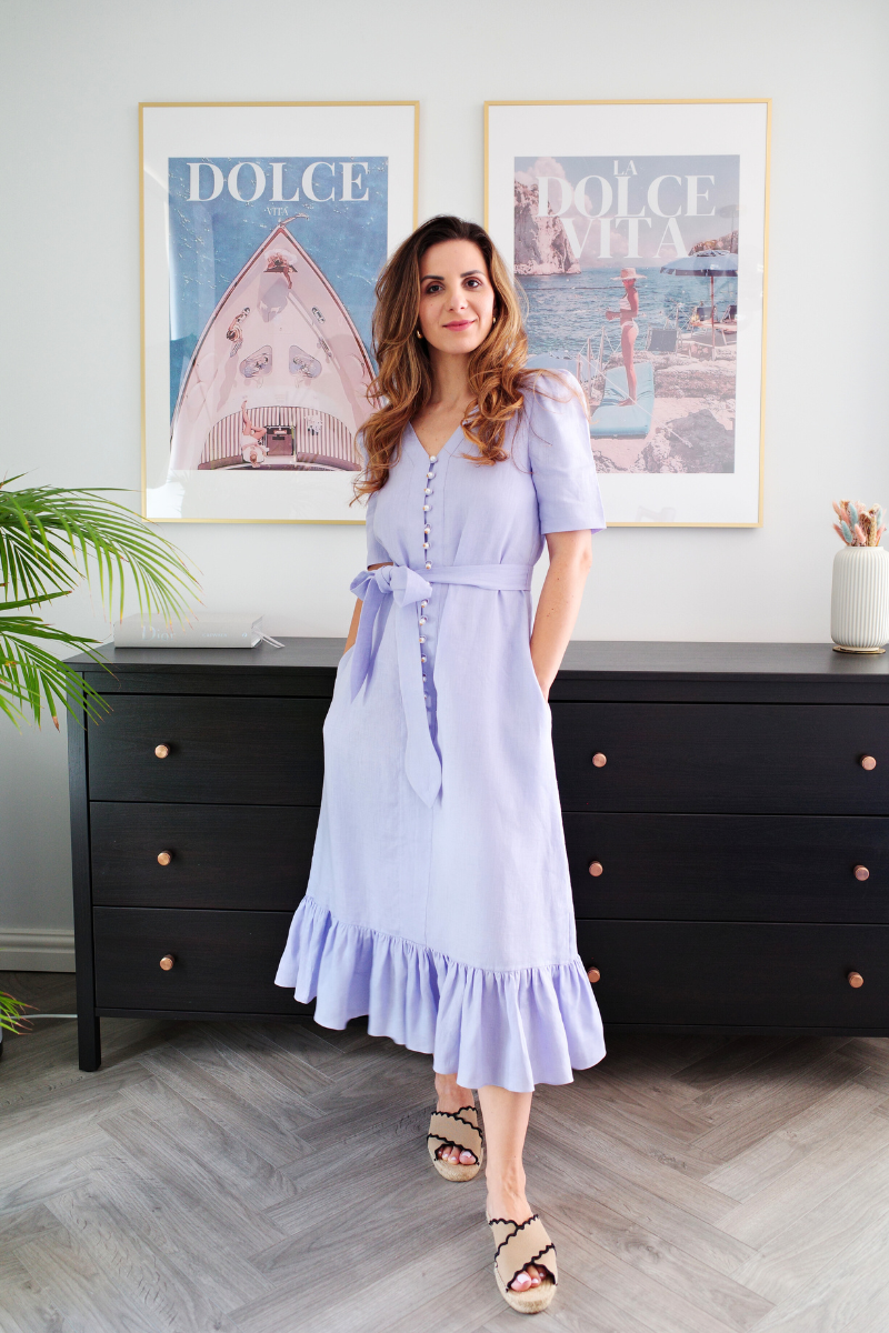 Woman in a light purple dress standing in a room with framed pictures on the wall.