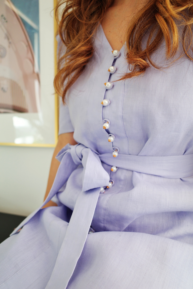 Close-up of a light purple dress with pearl buttons and a bow detail.